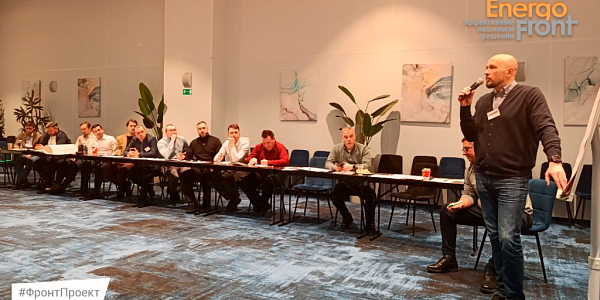 A speaker with a microphone speaks to a number of EnergoFront employees in a conference room