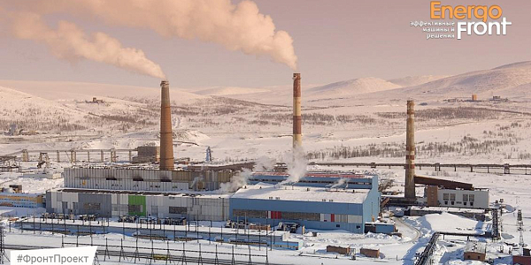 Winter view of a thermal power plant with three chimneys, smoke and a blue building among snowy hills