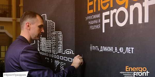A man in a suit writes a hashtag with chalk on the black wall of the EnergoFront stand