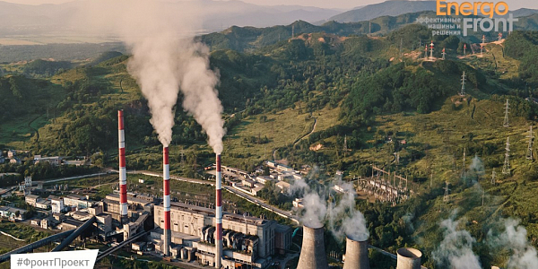 Aerial view of a thermal power plant with three striped chimneys and cooling towers in green hills