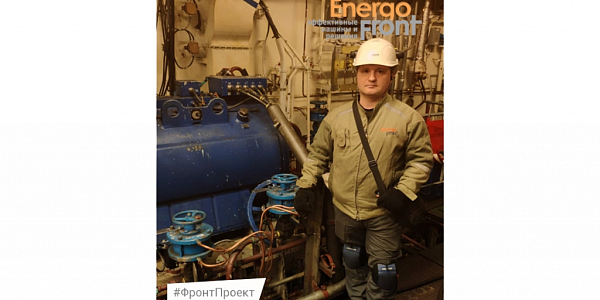 An engineer in a helmet and overalls near a blue unit in the engine room