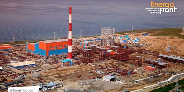 Coastal power facility under construction with red and white pipe and blue and orange body