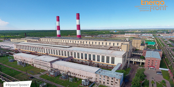 Aerial photograph of a long thermal power plant building with two striped pipes among fields