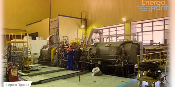Two specialists at a large gray cylindrical unit in a bright workshop