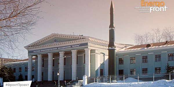Winter facade of NPO Iskra with columns and a rocket monument in front of the building