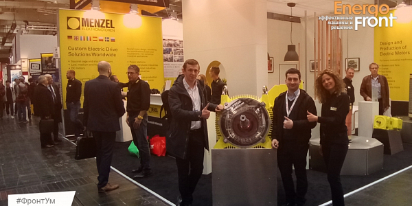 Three specialists at the yellow MENZEL electric motor at the exhibition stand