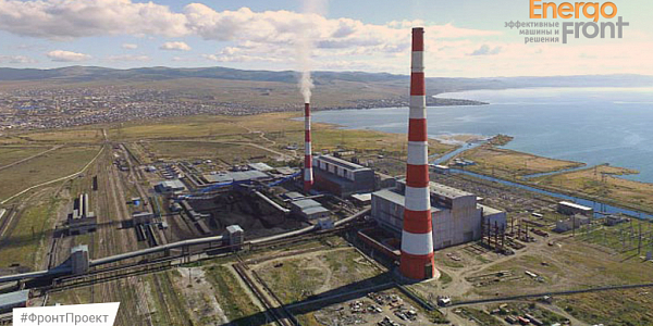 Aerial photograph of a coastal power plant with striped pipes near a large reservoir